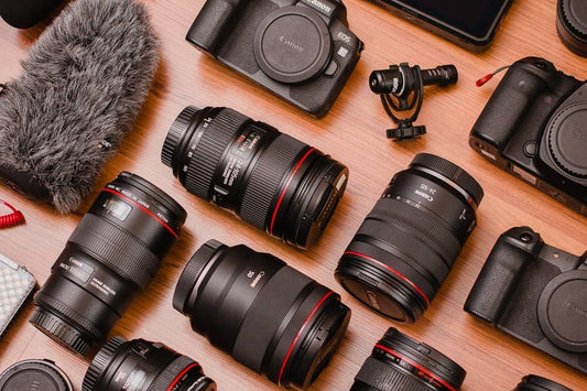 A variety of camera equipment, including different lenses, a camera body, and other photography accessories, arranged on a wooden surface.