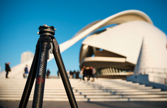 A tripod in front of a modern building with a blue sky and people in the background