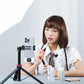 Woman using smartphone on tripod with lavalier microphone for makeup tutorial.